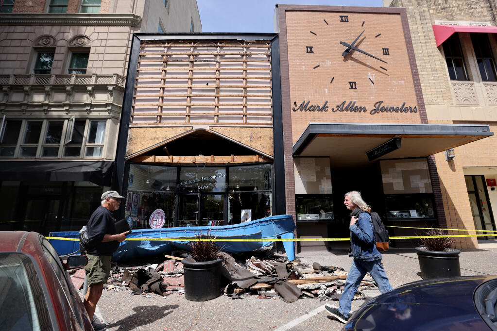 Pedestrians walk on Fourth St. past the California Luggage Company after the building's facade and awning fell onto the sidewalk across from Old Courthouse Square in Santa Rosa, California, on Sunday, April 3, 2022. (Beth Schlanker/The Press Democrat)