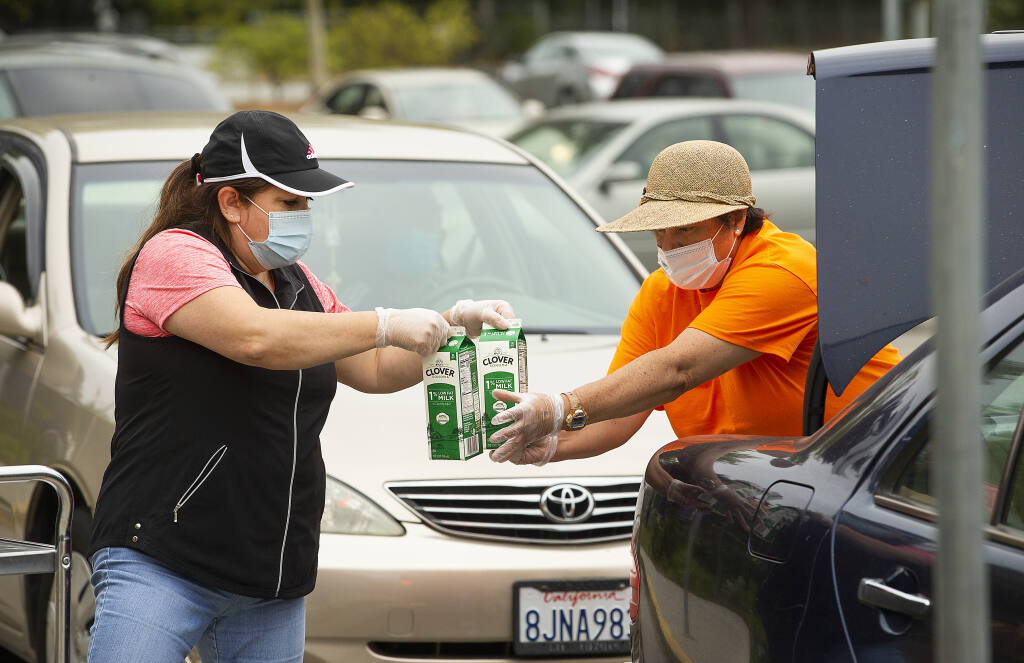Marta Guerra, left, and Sara Trejo load milk and food into cars for families enrolled in the free or reduced-price lunch program in Santa Rosa City Schools district at James Monroe Elementary School on Tuesday, Sept. 1, 2020.  (John Burgess / The Press Democrat)