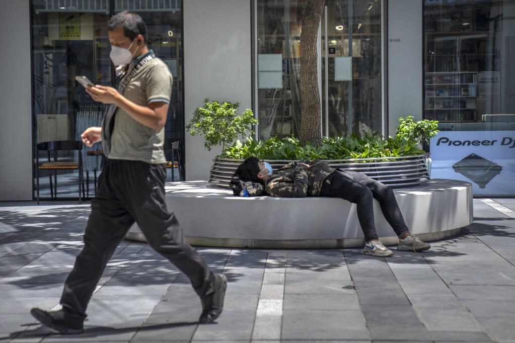 A man wearing a face mask takes a nap at a shopping and office complex in Beijing, Wednesday, June 1, 2022. (AP Photo/Mark Schiefelbein)