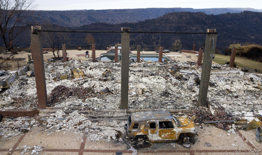 FILE - In this Dec. 3, 2018, file photo, a vehicle rests in front of a home leveled by the Camp Fire in Paradise, Calif. Homeowners and renters in 22 northern California counties are guaranteed not to lose their property insurance policies over the next year after the state announced a moratorium on Monday, Sept. 20, 2021, for people who live near recent wildfires. Insurance Commissioner Ricardo Lara issued a temporary moratorium for about 325,000 policyholders who live near those wildfires. (AP Photo/Noah Berger, File)