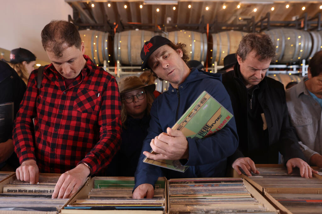 (From left) Jared Reeves, Townes Stanley, 11, his father Zac Stanley, and Rick Love thumb through boxes of records for sale during the Sonoma County Record Show, organized in partnership with Radiothrift and The NorCal Vinyl Society, at Shady Oak Barrel House in Santa Rosa, Sunday, March 19, 2023. (Beth Schlanker/The Press Democrat)