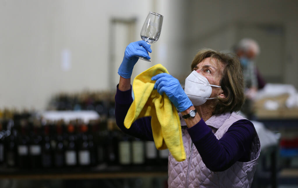 Vicki Michalczyk dries a glass while flights of wine are prepared for judging during the North Coast Wine Challenge in Santa Rosa on Tuesday, April 6, 2021.  (Christopher Chung/ The Press Democrat)