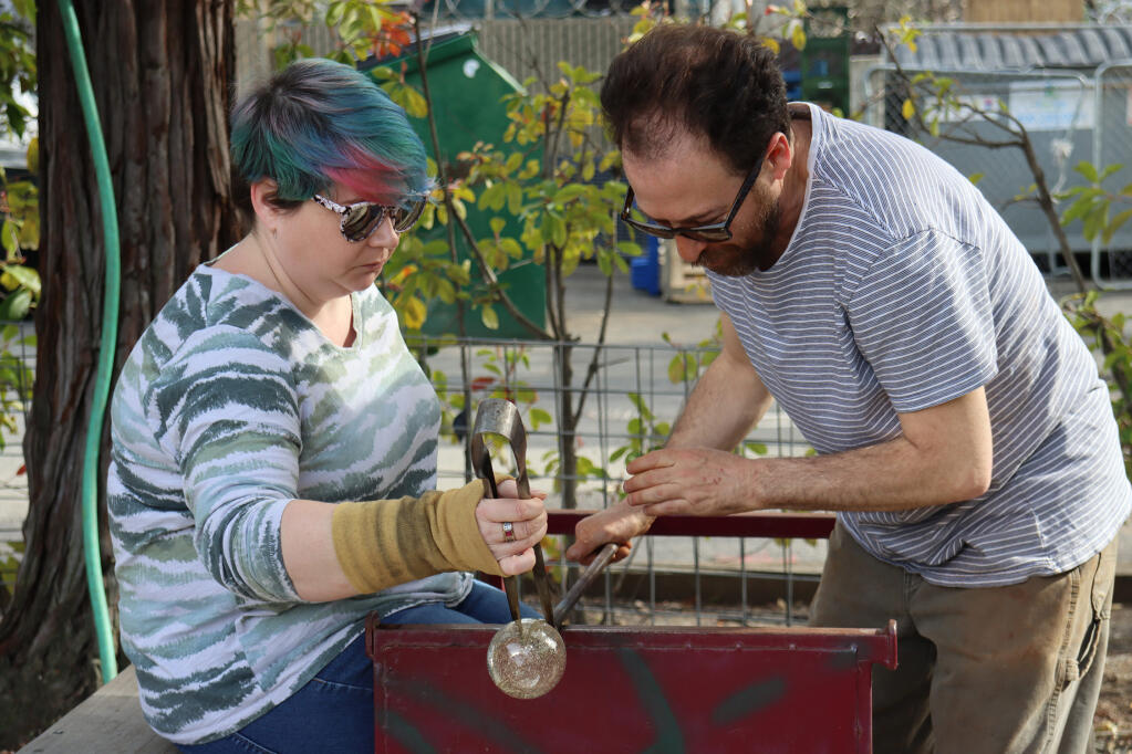 Alex Leader helps Kelly Grimsley with shaping the hot glass as he teaches a glassblowing class at Art Escape on Saturday, Feb.18, 2023.  (Liberty Olhava/for the Index-Tribune)