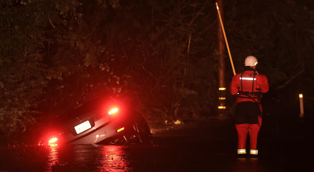 A Sonoma County Fire District swift water rescue firefighter  from Forestville, makes his way to a car in to a ditch on Eastside Road just south of Riverfront Regional Park near Forestville, Thursday, March 9, 2023. Several drivers were caught in floodwater, but all made it to safety. (Kent Porter / The Press Democrat)
