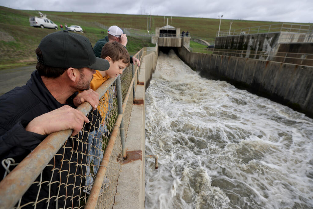 Mason Menton, 9, center, his dad, Laban Menton, left and family friend Blane Costello, rear, watch as water is released down the spillway at the Coyote Valley Dam at Lake Mendocino near Ukiah, Calif., Monday, January 16, 2023. (Beth Schlanker/The Press Democrat)