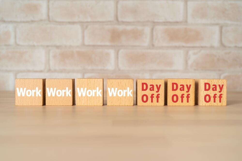 Wooden blocks with "Work" and "Day Off" illustrate the four-day workweek, with three days off.