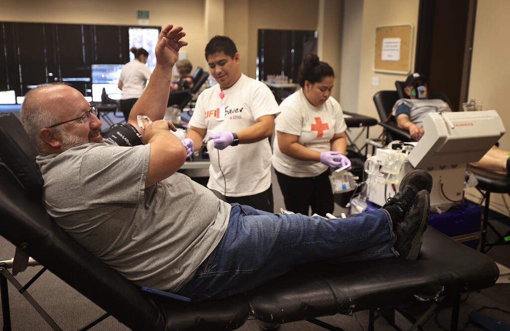 Larry Unsworth of Guerneville finishes up giving blood at the Red Cross in Larkfield, Saturday, July 3, 2021 as Red Cross employee Gerald Baniqued of San Leandro prepares to store the blood. Adolfo Gallo, right, waits to give blood as Erika Baniqued prepares the machinery. (Kent Porter / The Press Democrat) 2021
