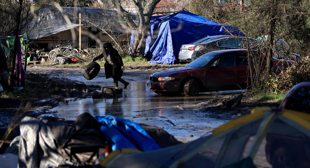 A woman at a homeless encampment on private property moves a tire so a motorist can leave, Saturday, Jan. 8, 2022 near the end of Old Stony Point Road in Santa Rosa. (Kent Porter / The Press Democrat) 2022