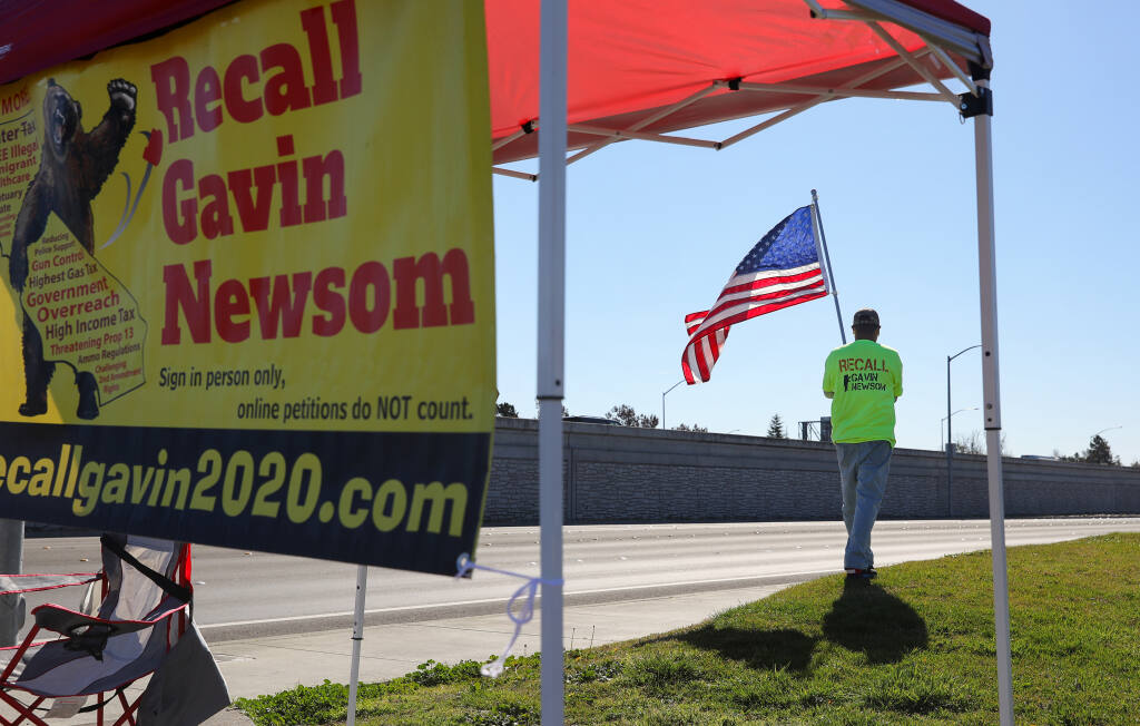 Jaime Ramirez posts a flag at the Recall Gavin Newsom petition station along Redwood Drive in Rohnert Park on Wednesday, Feb. 24, 2021. (Christopher Chung / The Press Democrat)