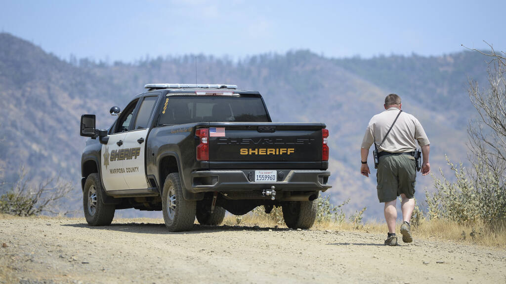 A Mariposa County deputy sheriff stands watch over a remote area northeast of the town of Mariposa, Calif., on Wednesday, Aug. 18, 2021, near the area where a family and their dog were reportedly found dead the day before. Investigators are considering whether toxic algae blooms or other hazards may have contributed to the deaths of the Northern California couple, their baby and the family dog on a remote hiking trail, authorities said. (Craig Kohlruss/The Fresno Bee via AP)