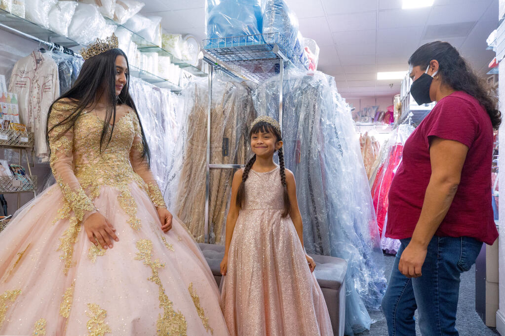 Myrian Rosas, 15, and her sister Soledad, 8, try on dresses for Myrian's quinceañera, while their mother Claudia, right, looks on, at Novedades Mexico in Petaluma. (Alvin A.H. Jornada / The Press Democrat)