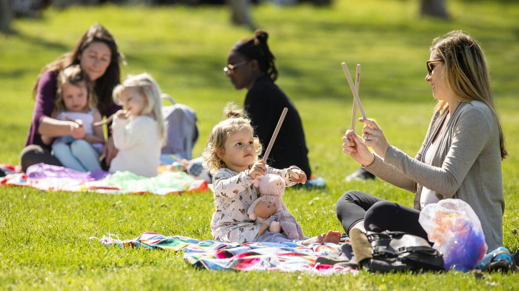 From left, mom Felice plays with twin daughter Sarah and Analise Toth, 2 1/2, along with Nonny Ndawo, while Liv, 2, shows her mom, Madison Hollander, how to make music with sticks during the Music Together music and movement outdoor class at the Healdsburg Community Center on Thursday, April 1, 2021. (John Burgess / The Press Democrat)