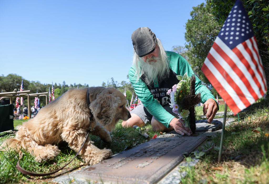 David Coe, with his dog Macy, places flowers at the graves of his parents, who both served in the Navy during World War II, and uncle, who served in the Army during World War II, at Cypress Hill Memorial Park in Petaluma on Monday, May 30, 2022.  (Christopher Chung/The Press Democrat)