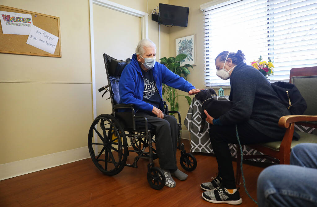 Tommy Phillips, left, pets Thunderbolt during a visit by his sister, Patty Feerick, at the Windsor Care Center of Petaluma on Friday, March 19, 2021.  The care facility set up a special visitation room for its care residents. (Christopher Chung/ The Press Democrat)