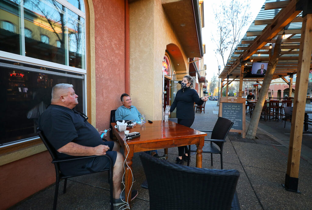 Waitress Megan Chiaretta, right, talks with customers Jens Shurk and Chuck Prindle at The Publican's outdoor dining area in Windsor on Thursday, December 10, 2020.  Sonoma County has announced a new round of restrictions that will go into effect at 12:01 a.m. Saturday.  (Christopher Chung/ The Press Democrat)