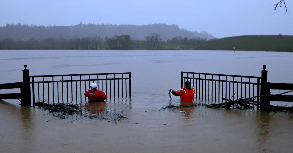 Firefighters with the Sonoma County Fire District open a gate to get their watercraft through prior to a search for vehicle submerged by floodwaters in a vineyard, Wednesday, Jan. 11, 2023, on Trenton-Healdsburg Road near Forestville. (Kent Porter/The Press Democrat)