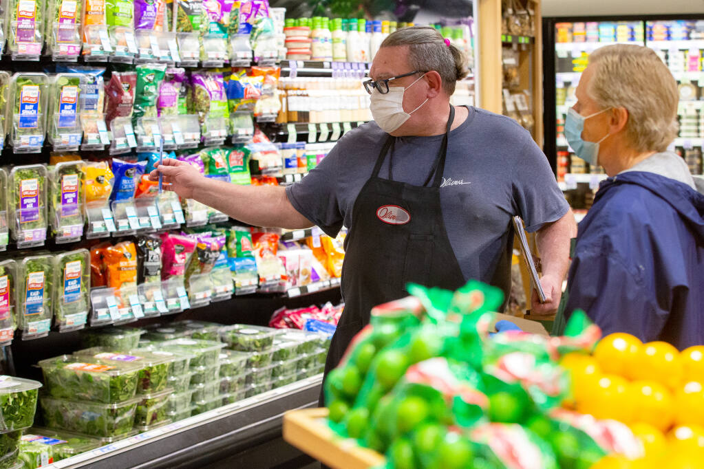 Produce department manager Rocket Burton, left, talks with clerk Douglas Kearns in front of the display of packaged greens at Oliver's Market in Windsor, California, on Tuesday, Jan. 12, 2021. (Alvin A.H. Jornada / The Press Democrat)