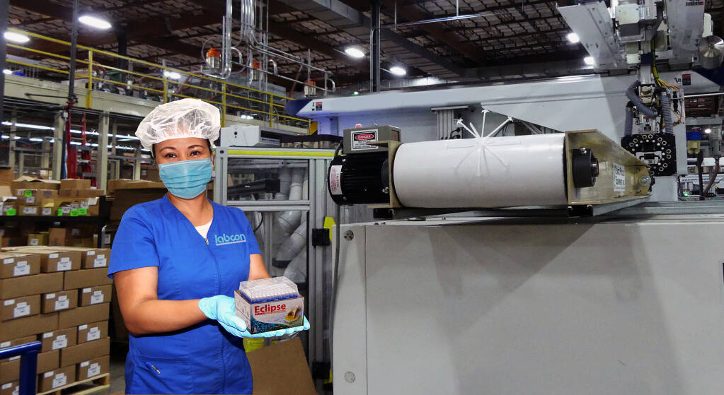 Nora Cuenca, a Labcon worker, stands is in front of a machine/robot combination which takes components and packages the finished product. Photo courtesy of Labcon