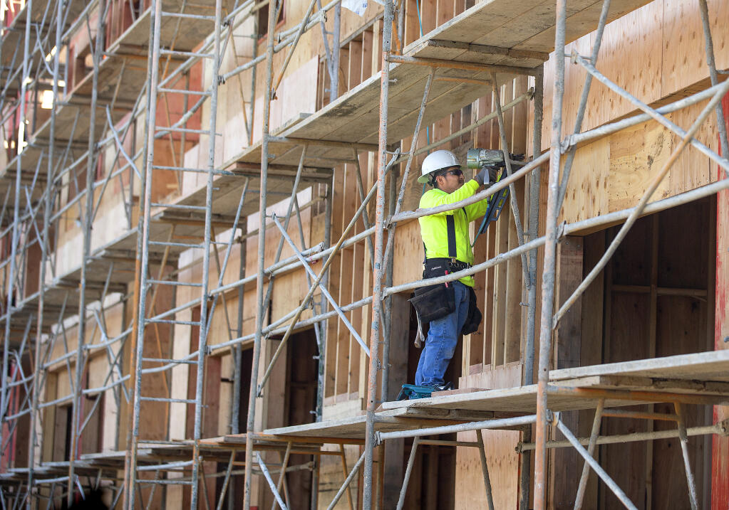 A worker uses a nail gun to attach plywood siding to the Dutton Flats project at 3rd Street and Dutton Ave. in Santa Rosa on Monday, March 1, 2021. The need for more affordable housing was cited Wednesday as a reason more people are leaving the state.  (Photo by John Burgess/The Press Democrat)