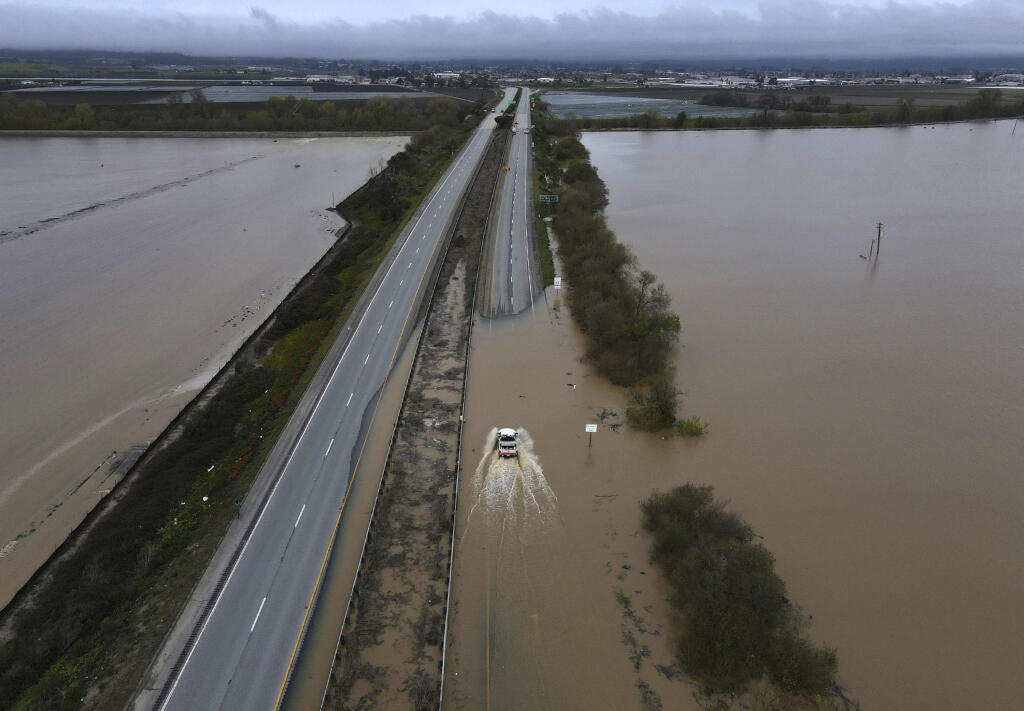A CalTrans vehicle drives north through floodwaters that closed state Highway 1 at the Santa Cruz County line, in California, Sunday, March 12, 2023. (Shmuel Thaler/The Santa Cruz Sentinel via AP)