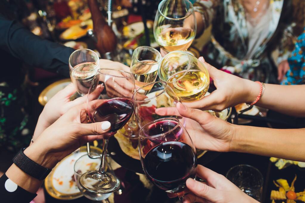 Seven people raise glasses of red and white wines for a toast at a restaurant.