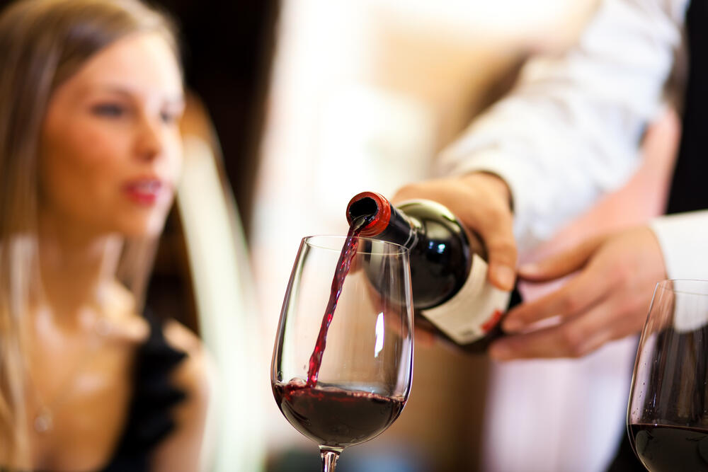 Waiter pours red wine for a woman in a restaurant. (Minerva Studio / Shutterstock)