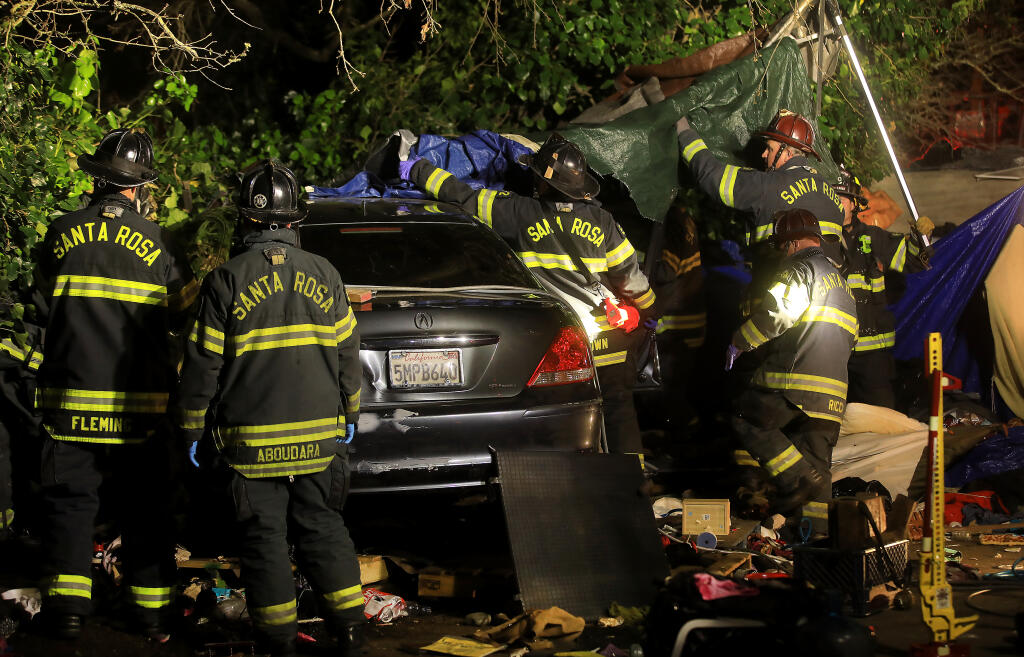 Santa Rosa firefighters clear the area around a car that plowed in to a homeless encampment in order to free a woman pinned underneath the vehicle on Roberts Avenue in Santa Rosa, Tuesday, March 23, 2021. (Kent Porter / The Press Democrat)