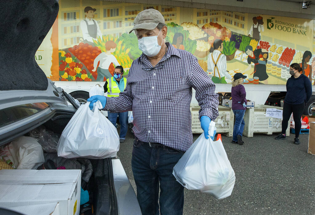 Zeke Guzman, President of Latinos Unidos del Condado de Sonoma, loads bags of food for people in needs while volunteering at the Redwood Empire Food Bank distribution on Wednesday evening, January 20, 2021.  (Photo by John Burgess/The Press Democrat)