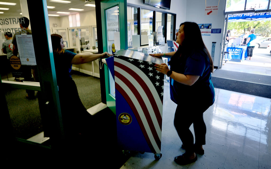 Julianne Goble, left, and Tegan Fossett of the Sonoma County Registrar of Voters move a ballot box in to the Registrar after it was filled with ballots by walk in voters, Tuesday, June 7, 2022 in Santa Rosa.   (Kent Porter / The Press Democrat) 2022