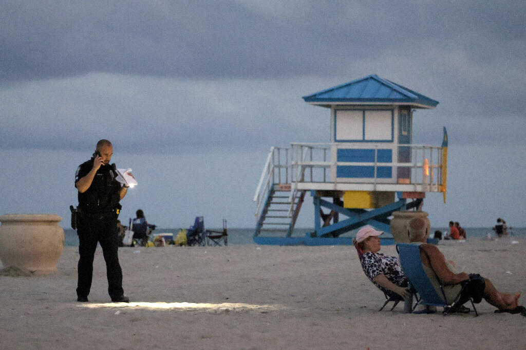 A police officer shines his flashlight downward as he pauses on Hollywood Beach while investigating a shooting Monday, May 29, 2023, in Hollywood, Fla. Multiple people were injured Monday evening when gunfire erupted along the beach boardwalk.  (Mike Stocker/South Florida Sun-Sentinel via AP)