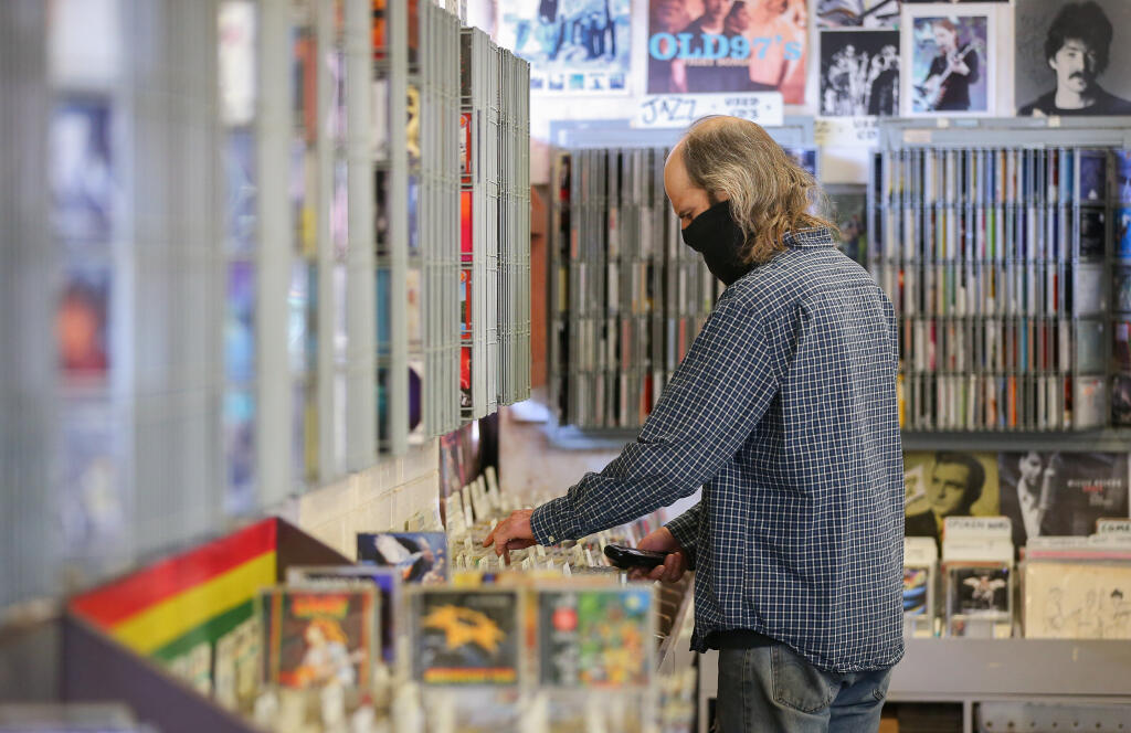 Michael "Hoyt" Wilhelm looks for a compact disc for a person on the phone at The Last Record Store in Santa Rosa on Tuesday, March 23, 2021. (Christopher Chung / The Press Democrat)