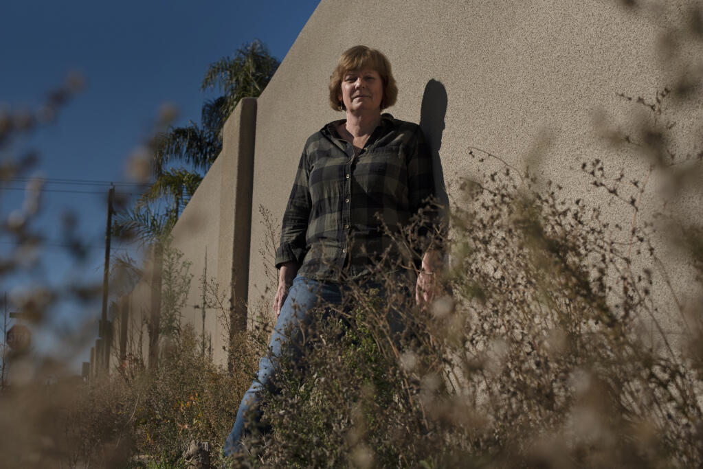 Coffey Strong Vice President Anne Barbour stands among the overgrown weeds and plants that have cluttered up the cracked and uneven sidewalk along the fire-resistant Hopper Avenue wall in the Coffey Park neighborhood of Santa Rosa on Wednesday, Dec. 23, 2020. (Erik Castro / For The Press Democrat)