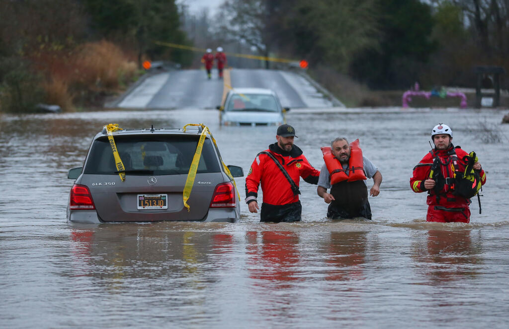 Sonoma County Sheriff’s Department Marine Unit Deputy Jacky Crachiola, left, and Sonoma County Fire District firefighter Chuck Franceschi, right, help a stranded motorist out of the flooded Slusser Road at River Road, near Windsor on Monday, Jan. 9, 2023. (Christopher Chung/The Press Democrat)