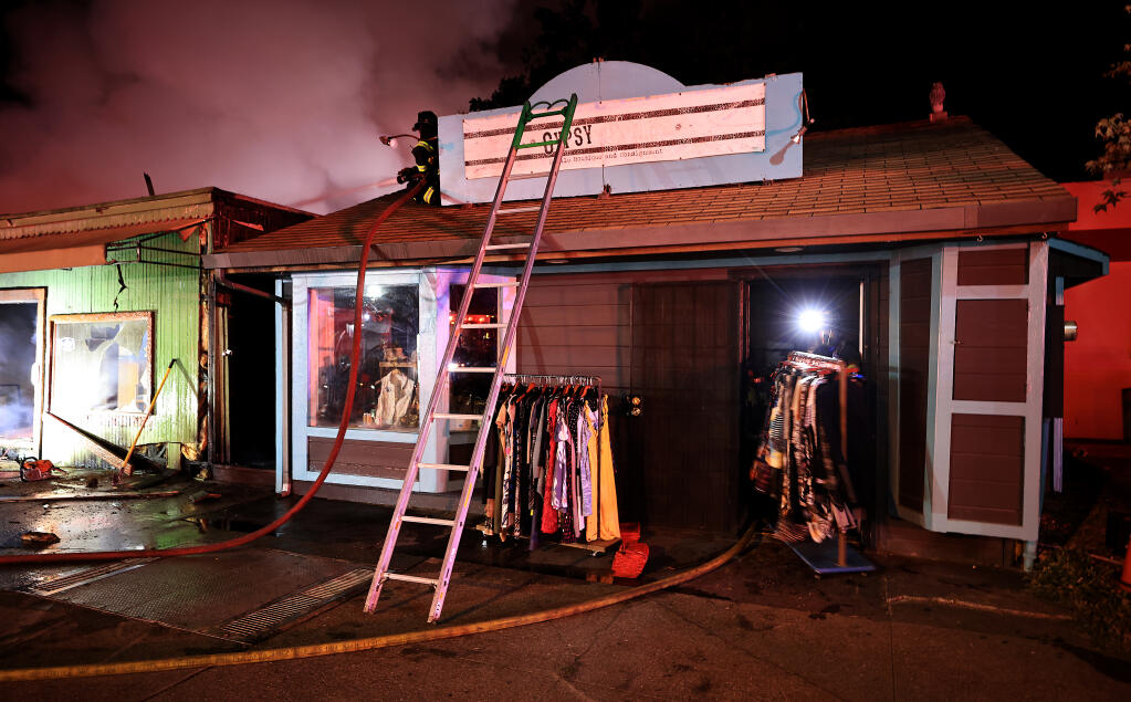 Merchandise is rolled out of Gypsy Sisters  so it wouldn't be damaged by water as firefighters work to contain a fire that burned three businesses along Guerneville's Main Street, late Sunday, Aug, 22, 2021. (Kent Porter / The Press Democrat)