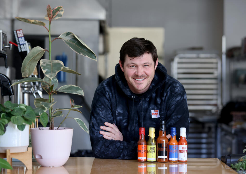 Andrew Whiting, founder and owner of Hot Drops, with a variety of flavors of hot sauce, including from left, Taco Boyz, JalaPasilla, Frique Pique, Not Sauce, and Fres-yes. Photo taken at Lunch Box in Sebastopol, Wednesday, March 8, 2023. (Beth Schlanker/The Press Democrat)