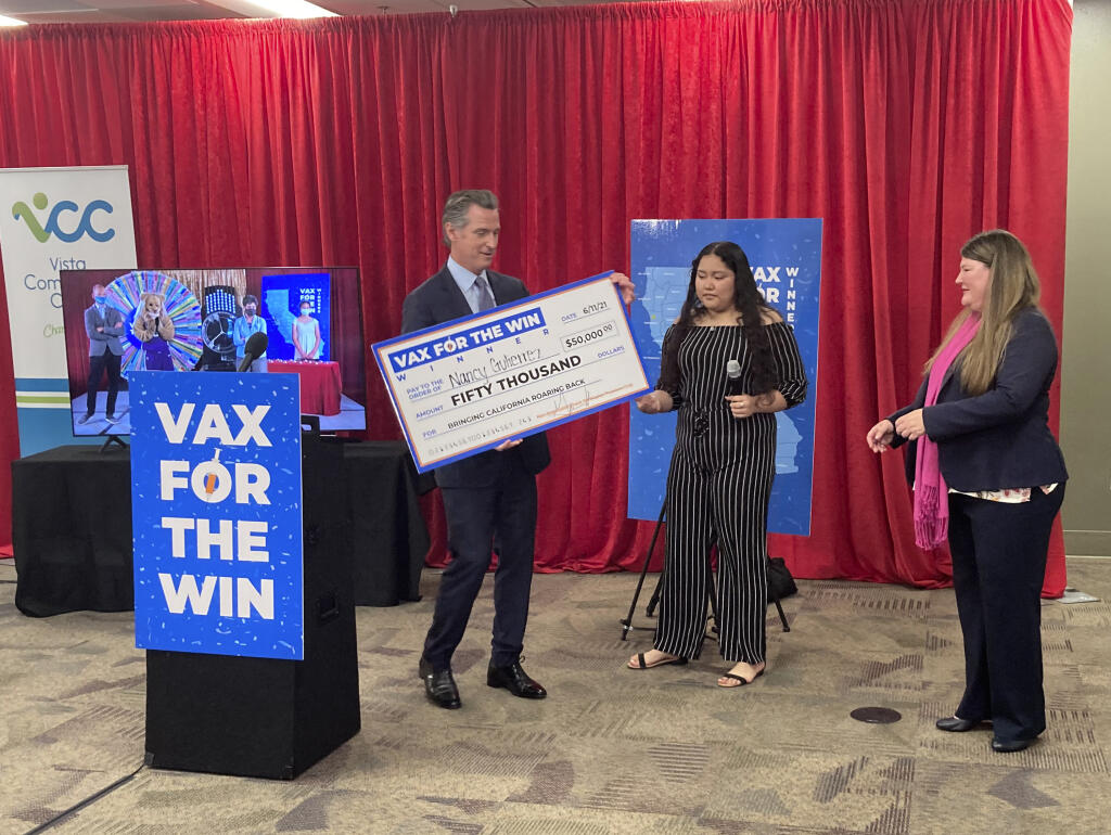 Gov. Gavin Newsom presents a check to Nancy Gutierrez, the winner of $50K lottery for getting vaccinated as Assemblywoman Tasha Boerner Horvath, right looks on in San Diego, Calif. on Friday, June 11, 2021. (AP Photo/Elliot Spagat)