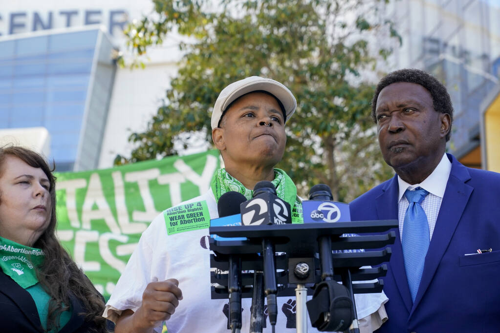 Kareim McKnight, center, talks to reporters during a press conference outside Chase Center, announcing the filing of a federal civil rights lawsuit against the San Francisco Fire and Police Departments in San Francisco, Wednesday, Aug. 10, 2022. McKnight alleges a paramedic, under the orders of a police sergeant, injected her with a sedative while she was handcuffed after protesting the Supreme Court's Roe v. Wade decision during a Golden State Warriors championship game. (AP Photo/Godofredo A. Vásquez)