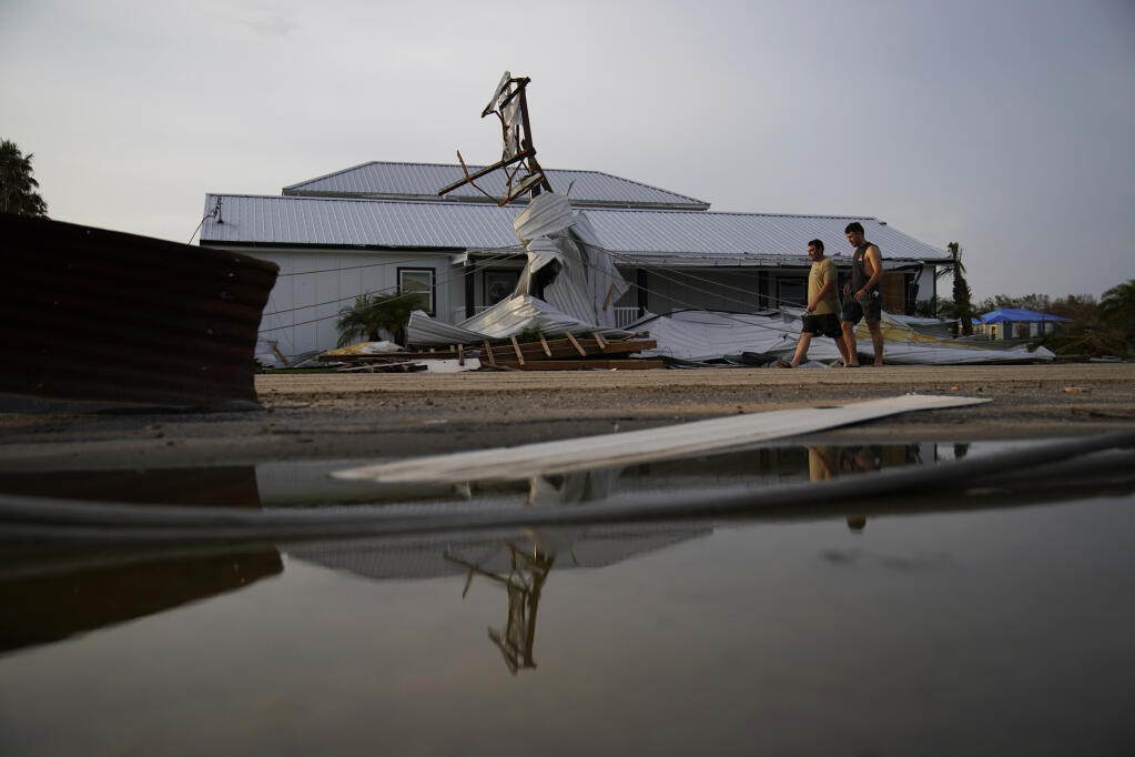People walk by buildings damaged by Hurricane Ida, Monday, Sept. 6, 2021, in Grand Isle, La. (AP Photo/John Locher)