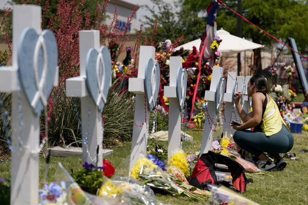 A woman signs a cross that stands by others at a makeshift memorial for the victims of a mass shooting, Monday, May 8, 2023, in Allen, Texas. (AP Photo/Tony Gutierrez)