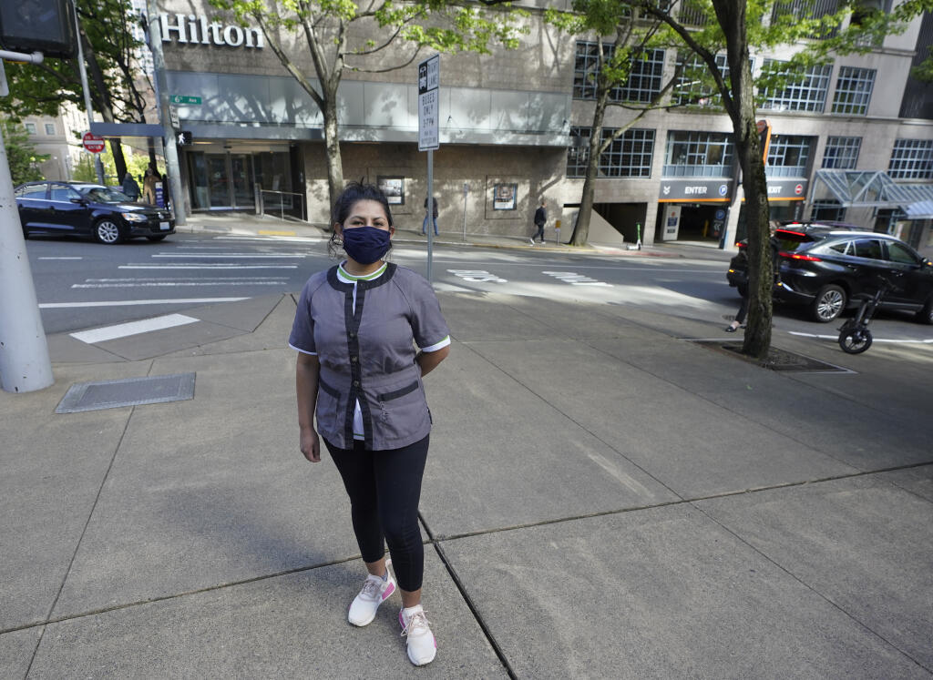 Sonia Guevara poses for a photo, Wednesday, May 18, 2022, outside the Hilton hotel where she works as a housekeeper in downtown Seattle. Many hotels across the United States have done away with daily housekeeping service, making what was already one of the toughest jobs in the hospitality industry even more grueling. (AP Photo/Ted S. Warren)