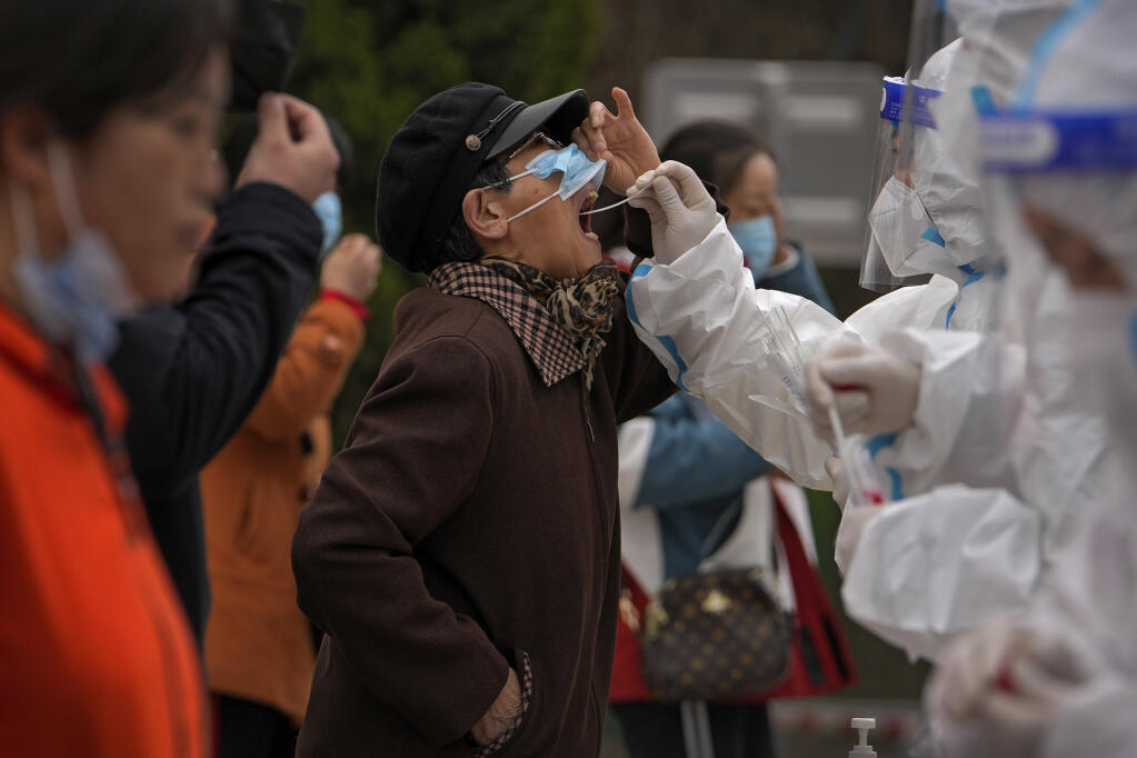 A health workers in protective suits takes a throat swab sample from a resident at a coronavirus testing site following a COVID-19 case detected Wednesday, April 6, 2022, in Beijing. (AP Photo/Andy Wong)