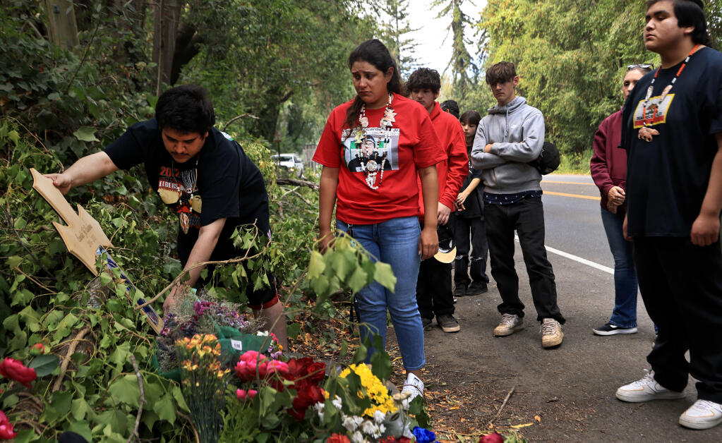 Antonio Cardenas, 25, with his sister, Isabelle Cardenas, place a cross, Thursday, Aug. 31, 2023, for their brother Oswaldo Mario-Rogelio Cardenas Jr., 18, at the River Road crash site where Cardenas Jr. was struck and killed by a hit-and-run driver Sunday.  At right is Nicandro “Nico” Cardenas, also a brother. (Kent Porter / The Press Democrat)