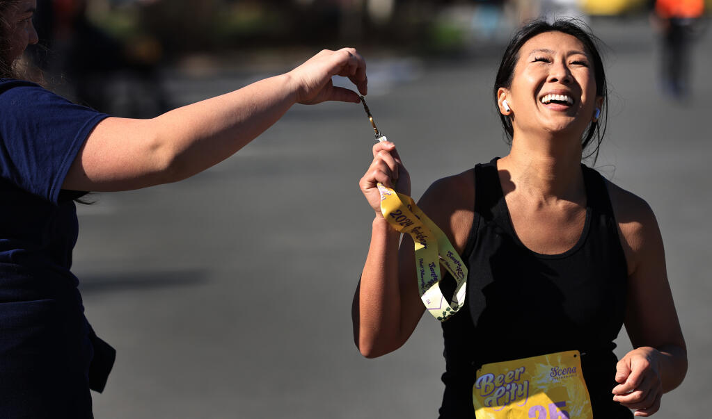 Santa Rosa resident Lily Hsieh receives a medal from Beer City volunteer Sherry Sanders of San Francisco, as she crosses the finish line during the Beer City Half Marathon, Saturday, Feb. 24, 2024,, at a Place to Play in Santa Rosa. Other mileage markers were a 10K and 5K and a 1-mile beer stroll.  (Kent Porter / The Press Democrat)