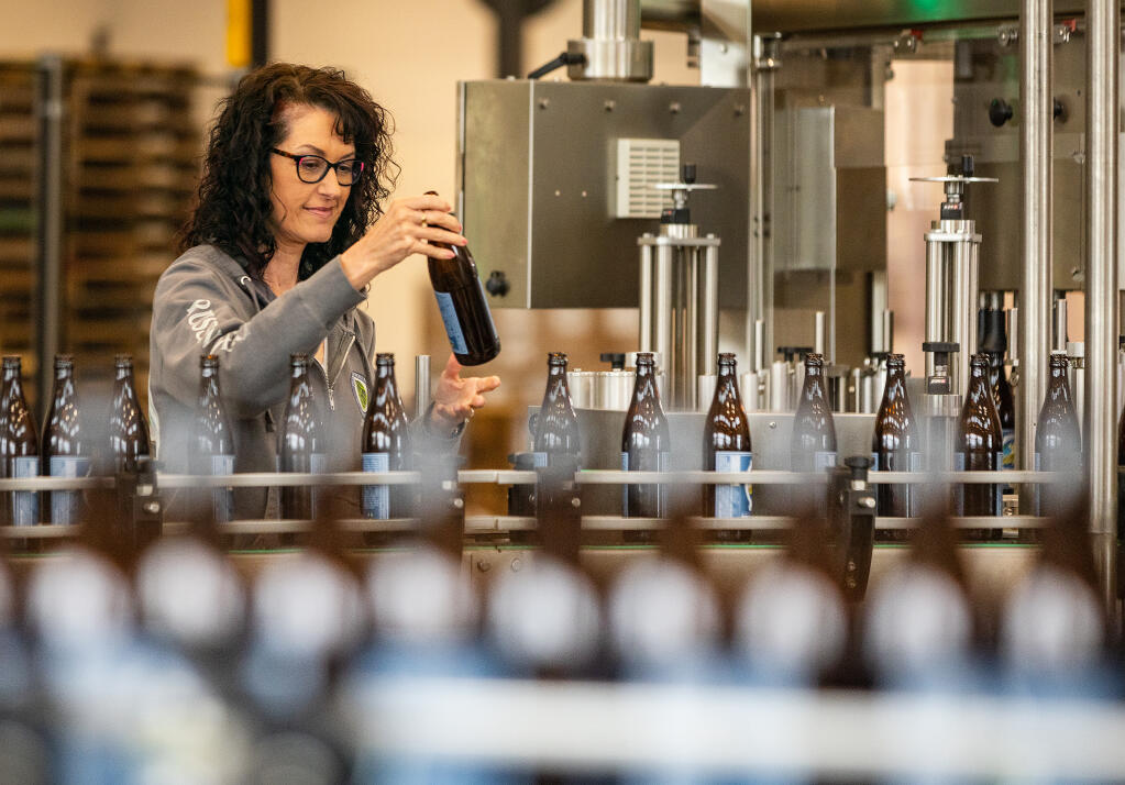 Russian River Brewing Co. co-owner Natalie Cilurzo pulls a bottle of the 20th anniversary 2024 Pliny the Younger triple IPA from the line so she can photograph it for a social media announcement of the release in Windsor, Tuesday, March 19, 2024. (John Burgess / The Press Democrat)