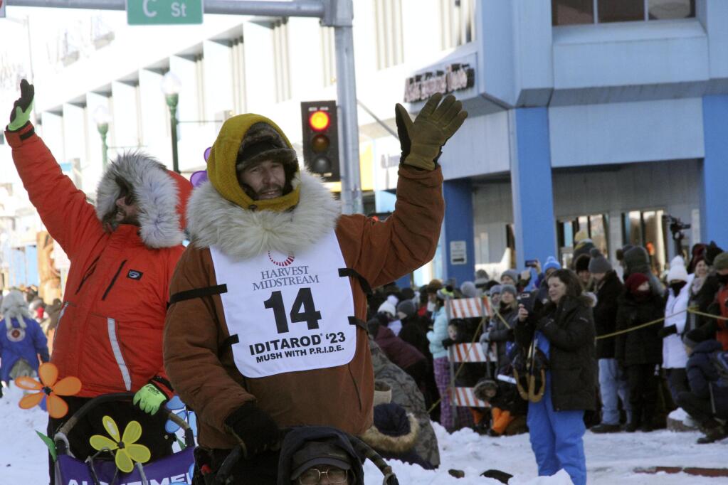Defending champion Brent Sass, wearing bib No. 14, waves to the crowd during the Iditarod Trail Sled Dog Race's ceremonial start in downtown Anchorage, Alaska, on Saturday, March 4, 2023. The smallest field ever of only 33 mushers will start the competitive portion of the Iditarod Sunday, March 5, 2023, in Willow, Alaska. (AP Photo/Mark Thiessen)