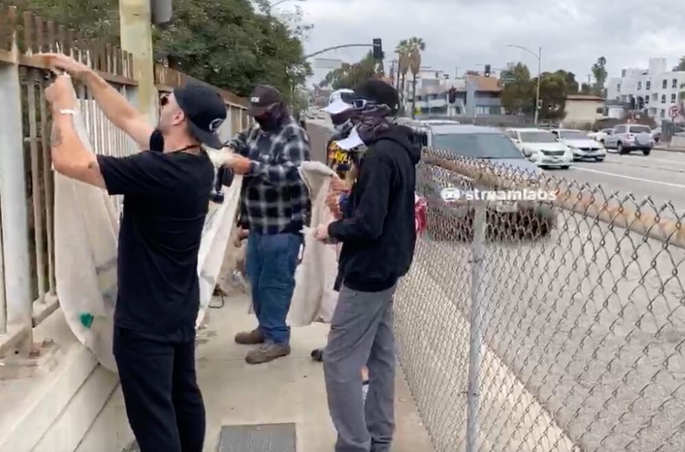 Jon Minadeo II (left) hangs an antisemitic banner over an I-405 freeway overpass in Los Angeles. California Gov. Gavin Newsom condemned the incident Monday. (Photo captured from Minadeo’s GoyimTV website)