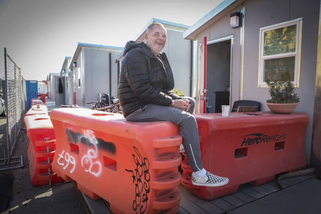 Bradley Brown smiles while sitting atop a makeshift barrier Tuesday, April 12, 2022, at the Petaluma People’s Village tiny home community. Brown was the first person to move into a tiny home at the People’s Village. (CRISSY PASCUAL/ARGUS-COURIER STAFF)