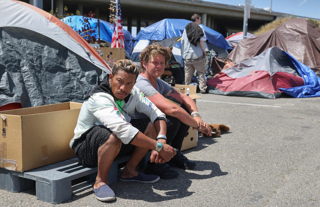 City-sanctioned homeless encampment residents Vanna An, left, and Elethea Kerivan sit and smoke at the camp along Roberts Lake Road in Rohnert Park on Monday, May 16, 2022. An is newly homeless and has been at the camp for two days, while Kerivan has lived at the camp for three months. (Christopher Chung/ The Press Democrat)