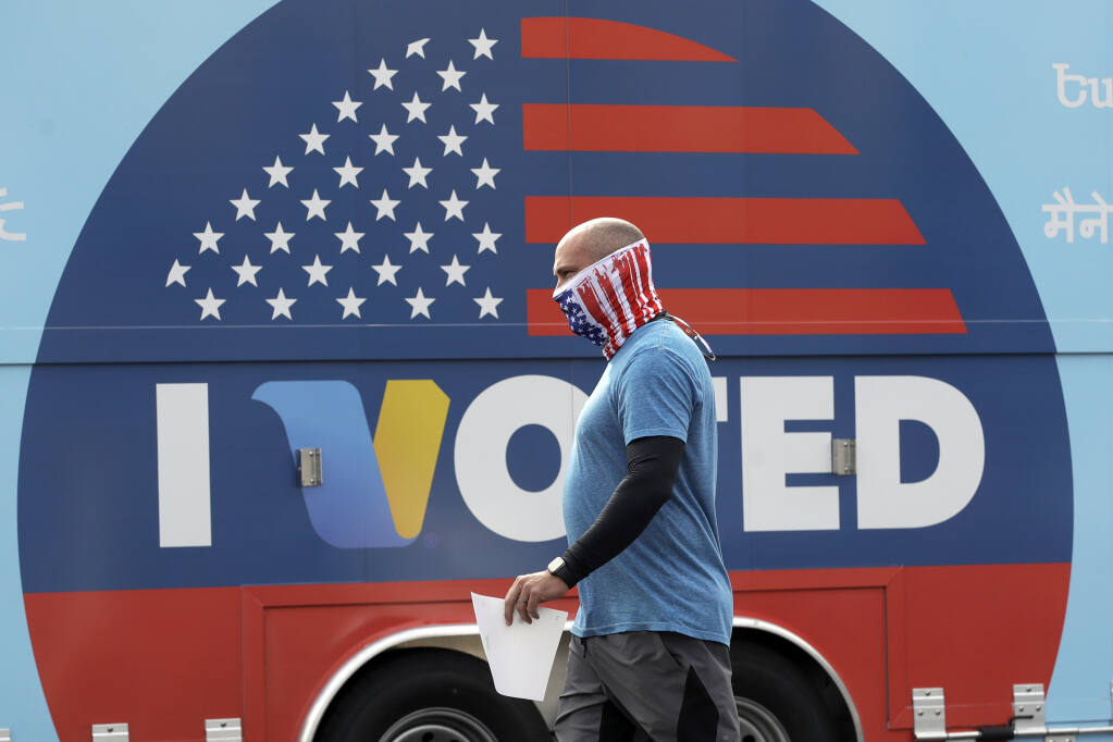 FILE - In this May 12, 2020 file photo, Robb Rehfeld wears a mask as he walks to cast his vote during a special election for California's 25th Congressional District seat in Santa Clarita, Calif.  With a divided nation on edge as Election Day approaches, California is warning local election officials to prepare for disruption at polling places and potential cases of voters being intimidated or blocked from casting ballots.  (AP Photo/Marcio Jose Sanchez, File)