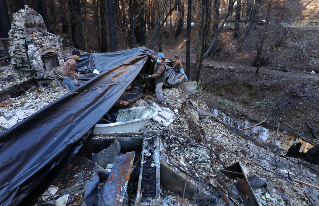 Jorge Tereta, left, and Alfredo Cuj, of Community Soil, place plastic sheets over a home destroyed by the Walbridge fire along Mill Creek Road, near Healdsburg, to help prevent hazardous materials from washing into the creek on Monday, Jan. 25, 2021.  (Christopher Chung/ The Press Democrat)